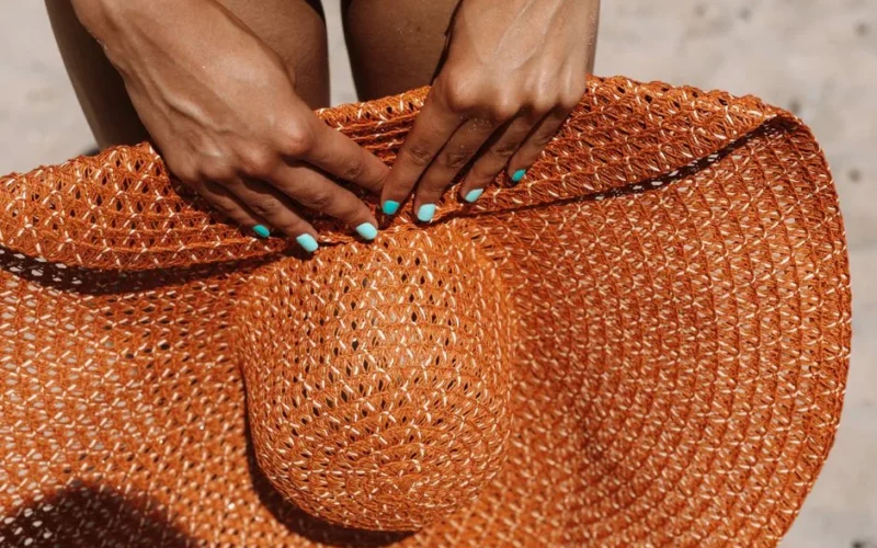 Detailed shot of hands with blue nails holding a woven sun hat outdoors.