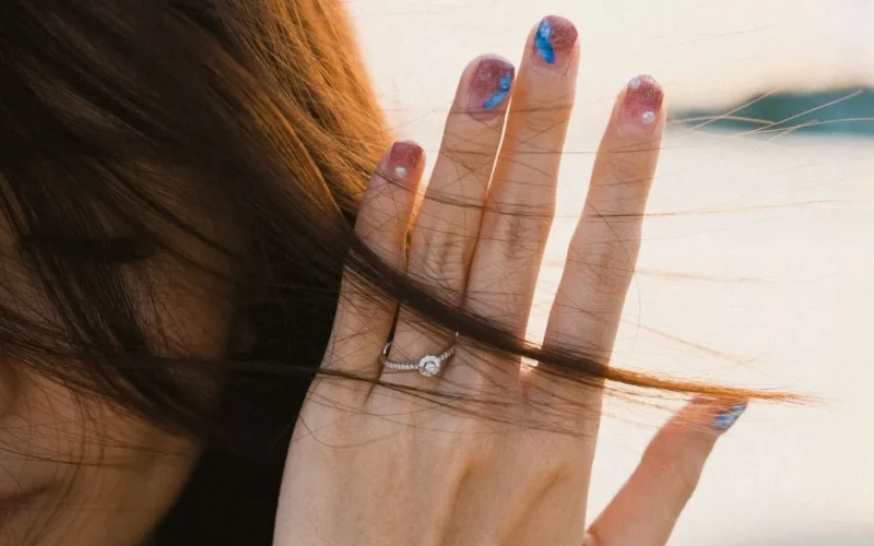 A hand with colorful nail art and a sparkling ring is captured against a soft background.