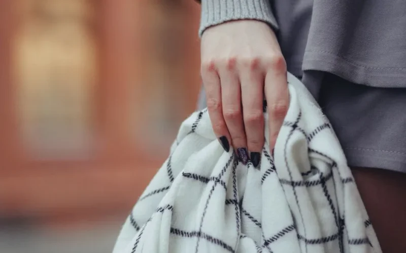 A woman's hand with intricate nail art holding a patterned blanket in a stylish close-up shot.