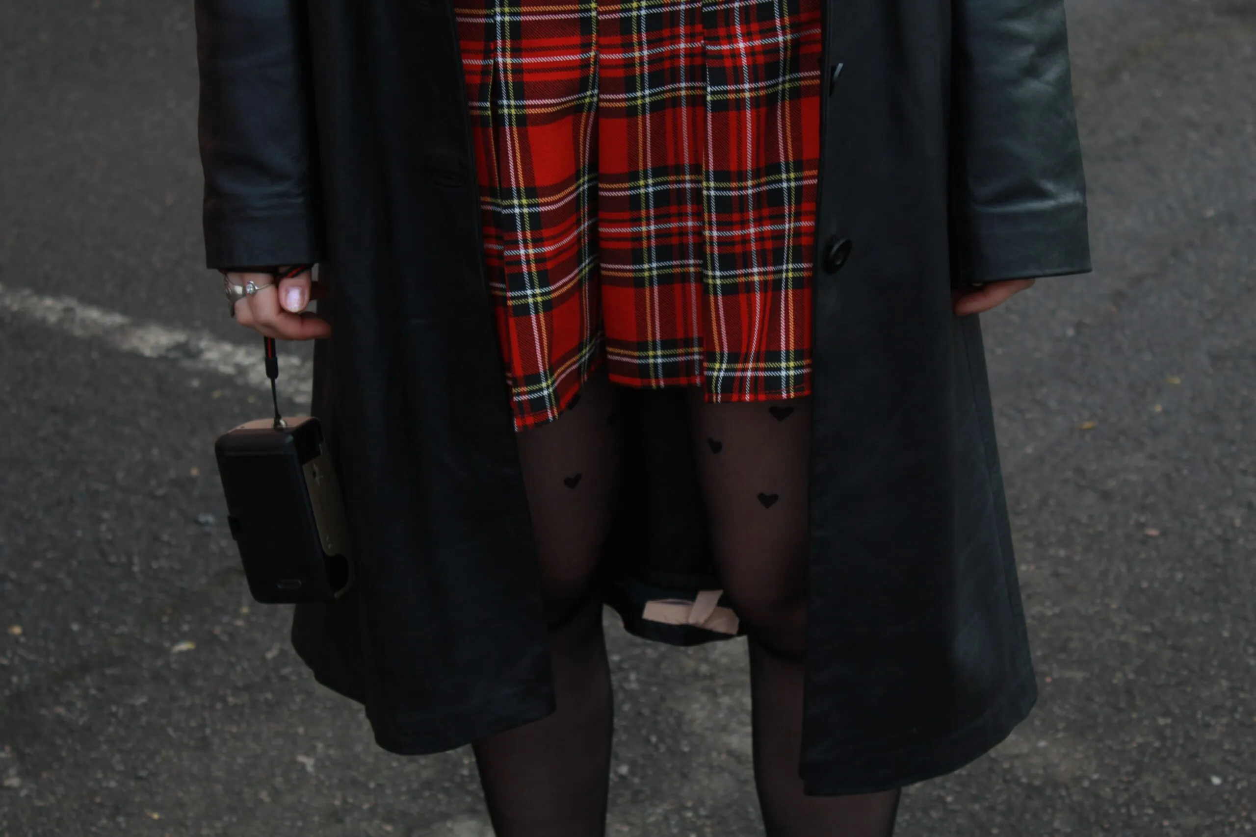 Close-up of a woman in a plaid skirt and leather jacket holding a vintage camera.