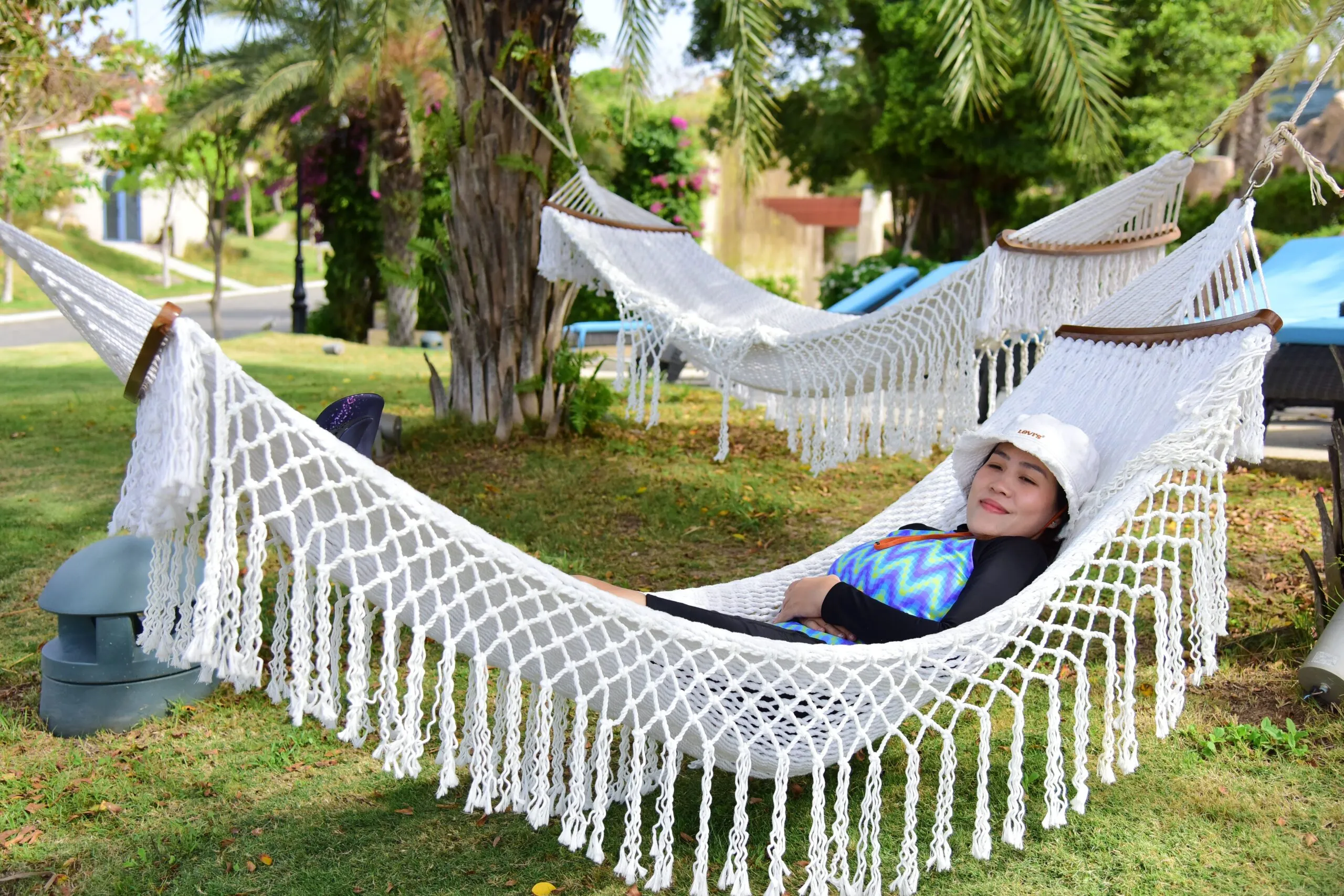 A woman enjoys a peaceful afternoon on a hammock in a sunny park with palm trees.