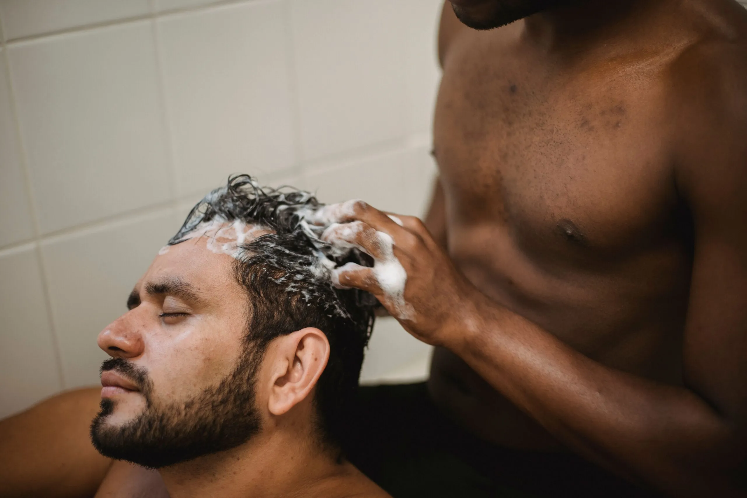 An intimate moment of a couple washing hair with care and affection in a bathroom setting.