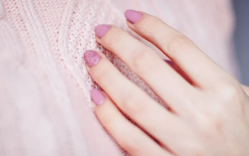 Close-up of a woman's hand with pink manicure resting on a soft knit sweater, showcasing elegance and fashion.