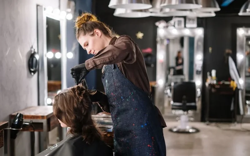 A female stylist expertly applying hair color to a client in a modern salon setting.