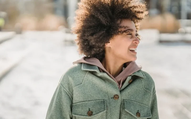Laughing ethnic woman with dark curly hair in warm outerwear looking away while strolling outdoors in wintertime