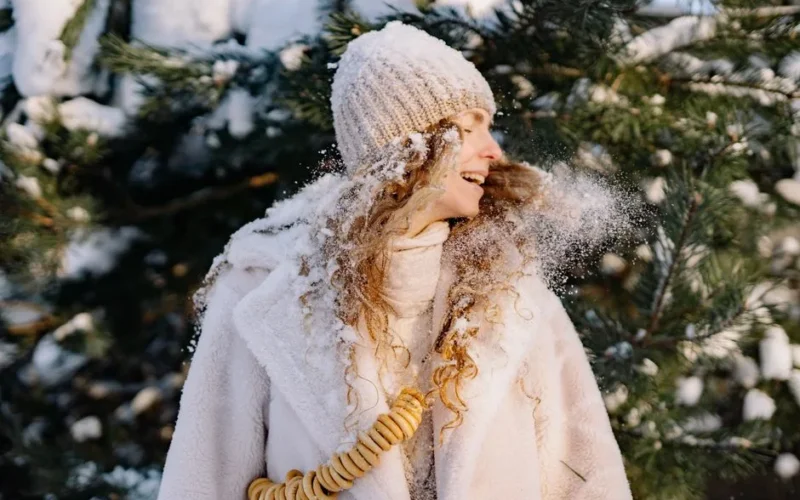 Happy woman with curly hair and knitted cap enjoying a snowy winter day outdoors.