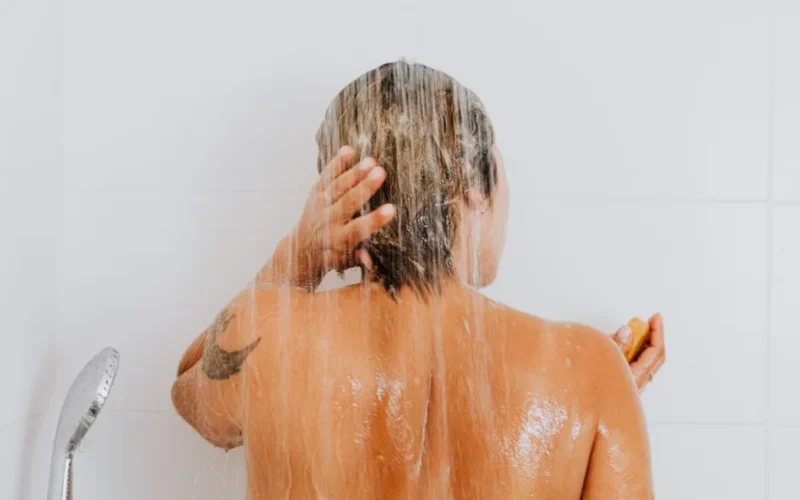 Rear view of a woman rinsing hair under shower, capturing an intimate and refreshing moment indoors.
