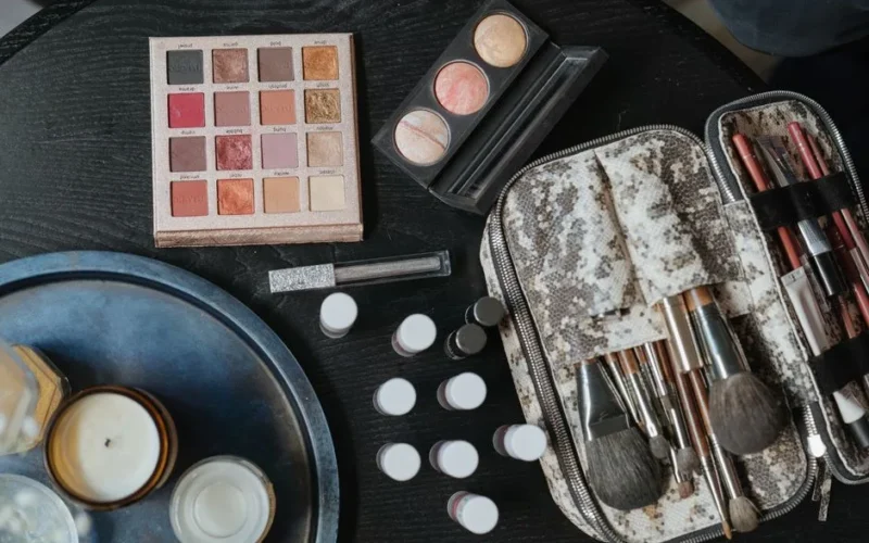 High-angle shot of cosmetics including brushes and an eyeshadow palette on a dark surface.