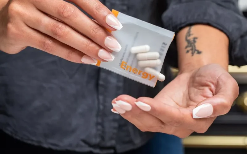 Close-up of woman's hands holding a packet of energy supplement capsules.