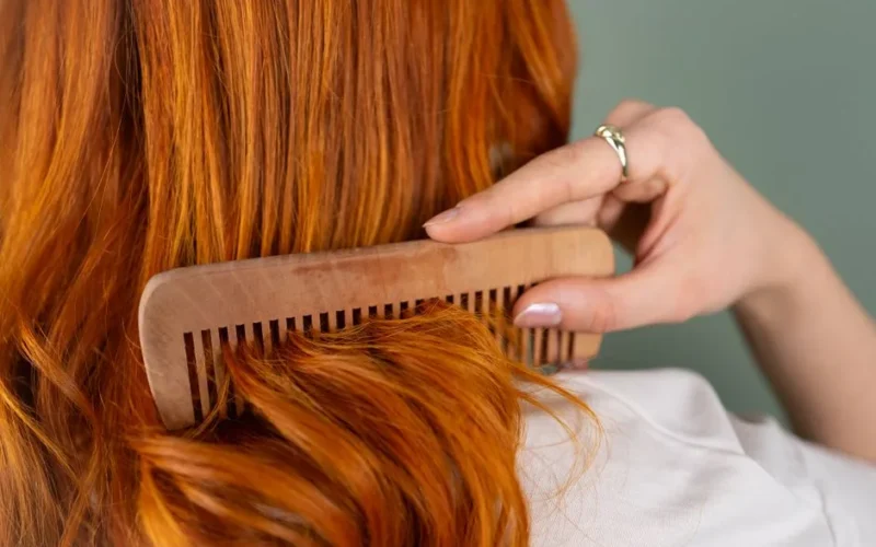 Close-up of a woman combing her long red hair with a wooden comb.