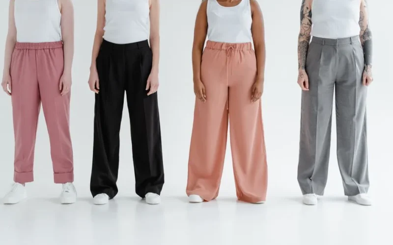 Four women stand in colorful trousers against a white background, showcasing diversity and fashion.