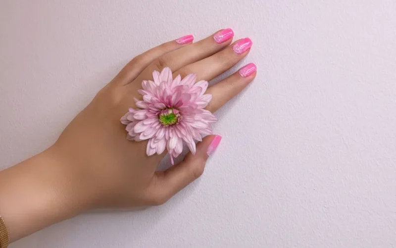 Close-up of a woman's hand with pink nails and a pink flower, showcasing delicate beauty.