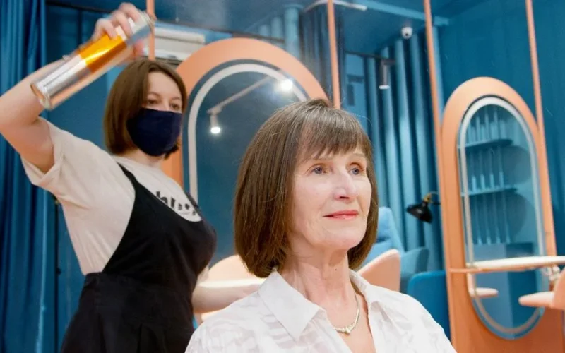 A hairstylist applies hairspray to a senior woman's new hairstyle in a modern salon.