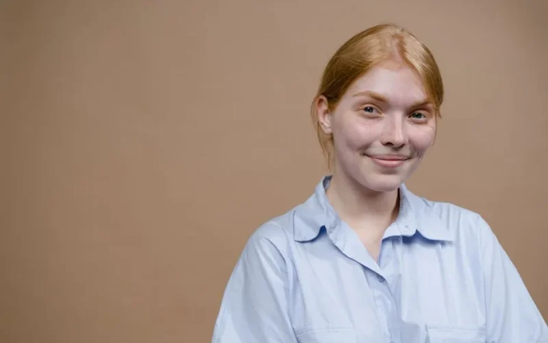Caucasian woman with blonde hair smiling against a beige background in a studio setting.