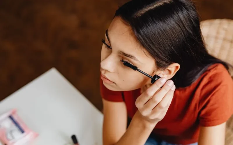 Close-up of a young woman applying mascara indoors, focusing on beauty routine.