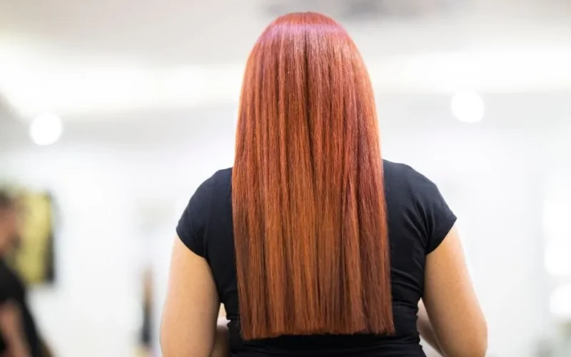 A woman with straight, vibrant red hair seen from the back, showcasing a fresh hairstyle in a professional salon.