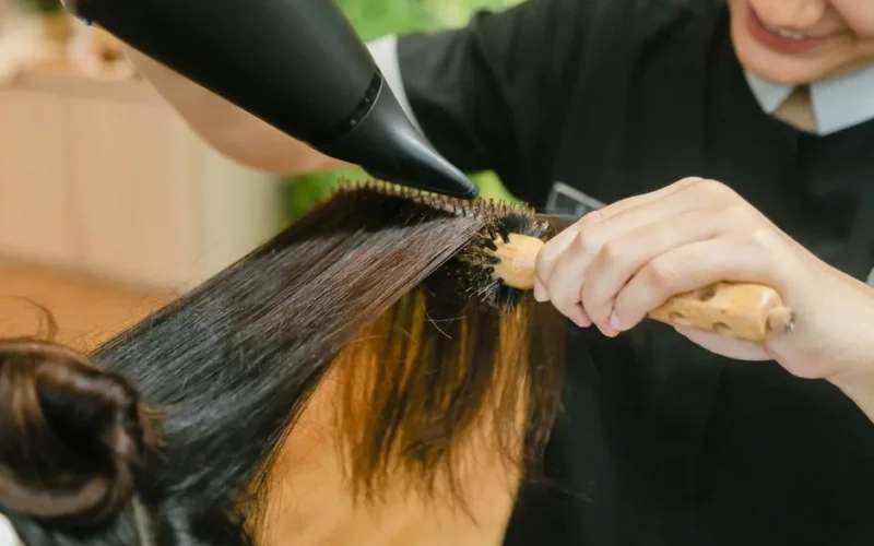 Close-up of hair stylist using a hairdryer and brush to style long hair.