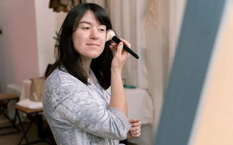 Teenage girl applying makeup indoors, enhancing her natural beauty.