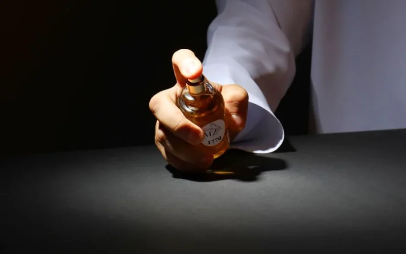 A hand elegantly holding a perfume bottle against a dark backdrop, highlighting luxury fragrance.