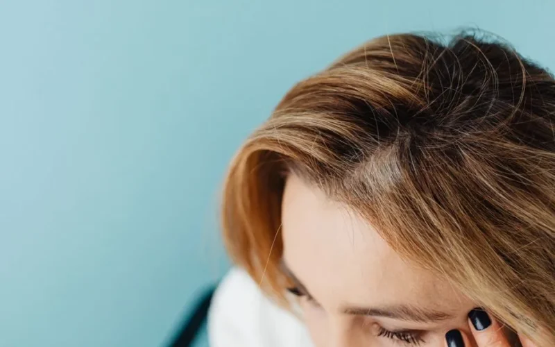 Close-up of a woman with a hand on forehead against a blue background.