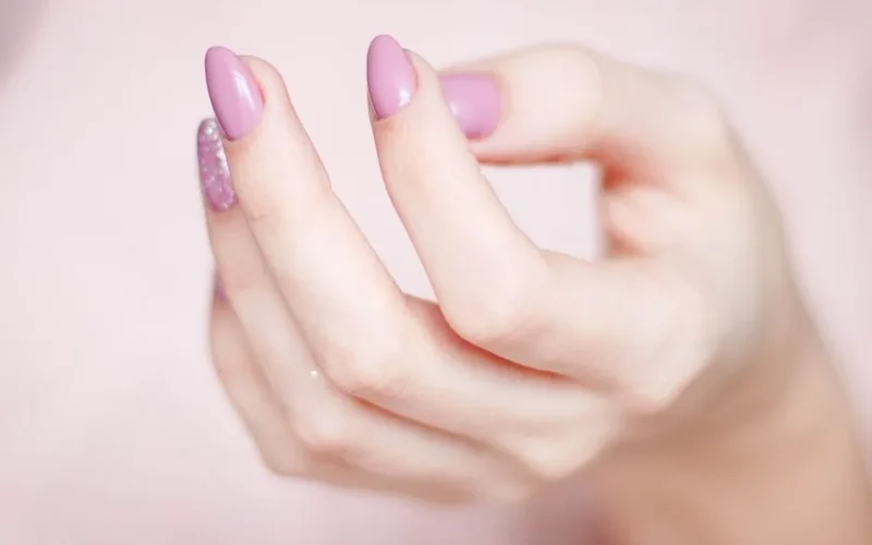 A close-up of a woman's hand showing a stylish pink and glittery manicure.