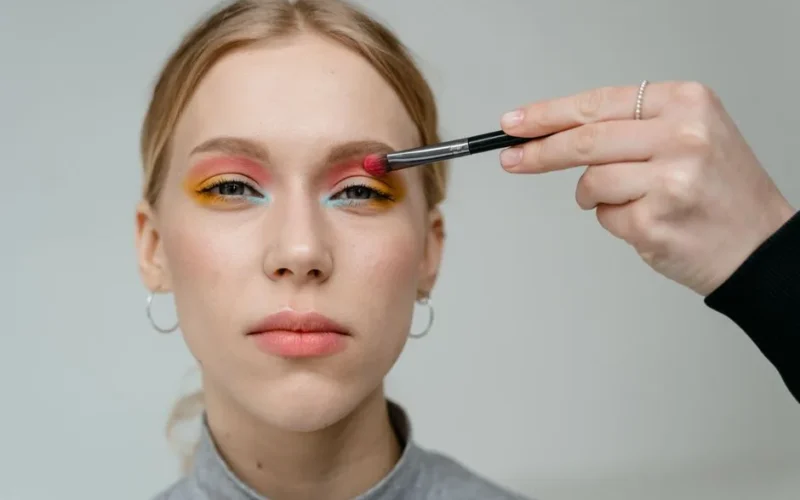 Close-up portrait of a woman with vibrant eyeshadow applied with a brush.