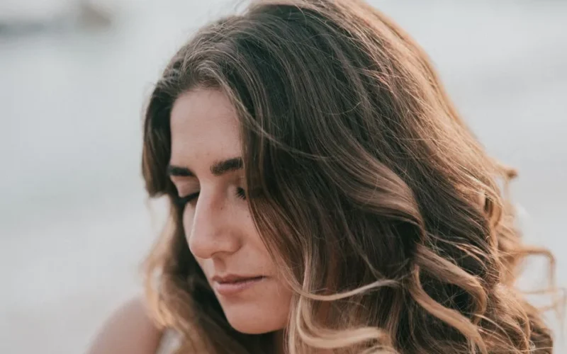Close-up portrait of a young woman with wavy blonde hair and eyes closed, conveying serenity.