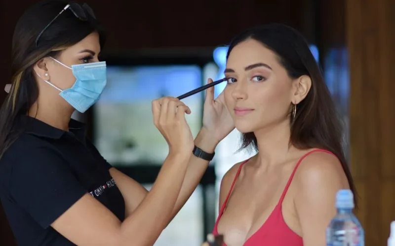 A makeup artist applies eye makeup to a woman indoors, highlighting beauty and precision.