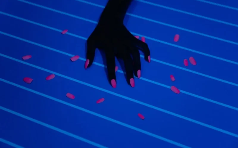Artistic photo of a hand with neon nails scattered with pills on an ultraviolet background.