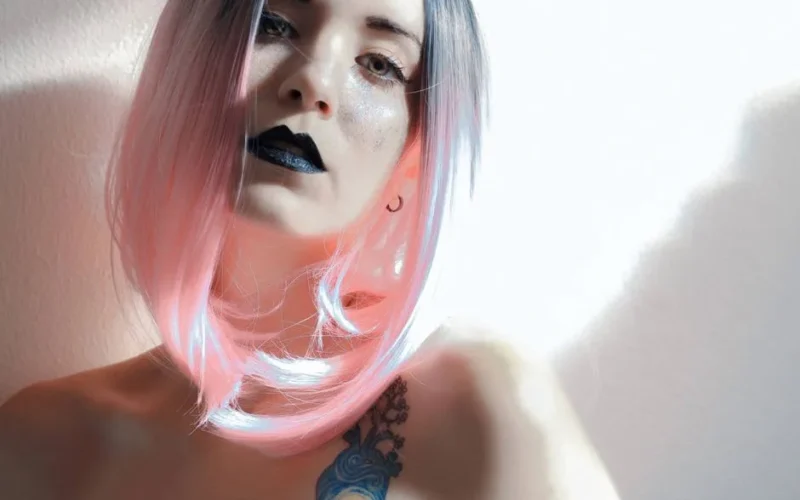 Artistic portrait of a woman with pastel ombre hair and tattoos in soft light.