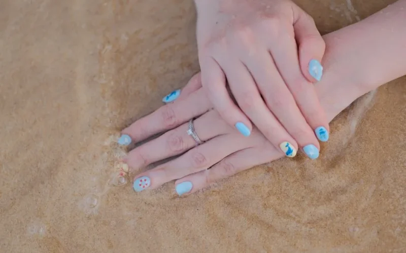 A serene close-up of hands with beach-themed nail art against sandy beach waves.