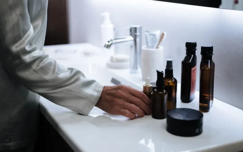 A hand reaching for skincare products on a modern bathroom sink.