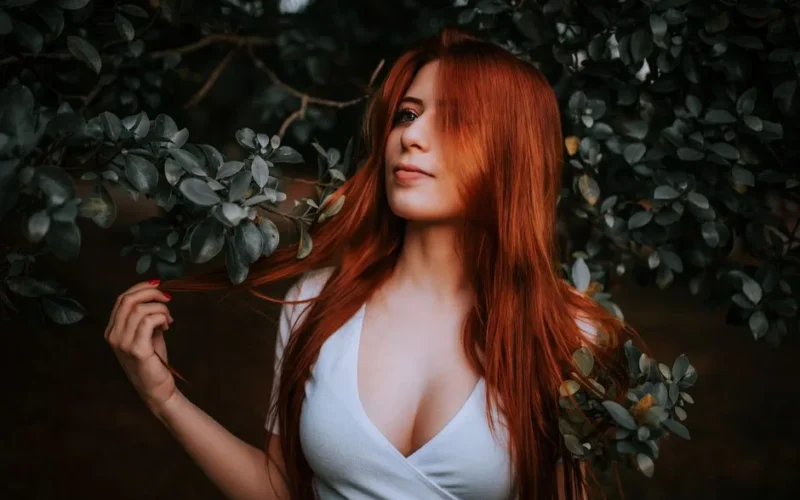 Close-up portrait of a red-haired woman surrounded by greenery, embodying natural beauty.