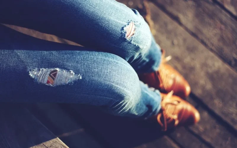 Close-up of stylish ripped jeans paired with brown leather shoes outdoors.