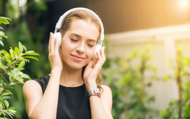 Smiling woman listening to music with headphones in sunny garden setting.