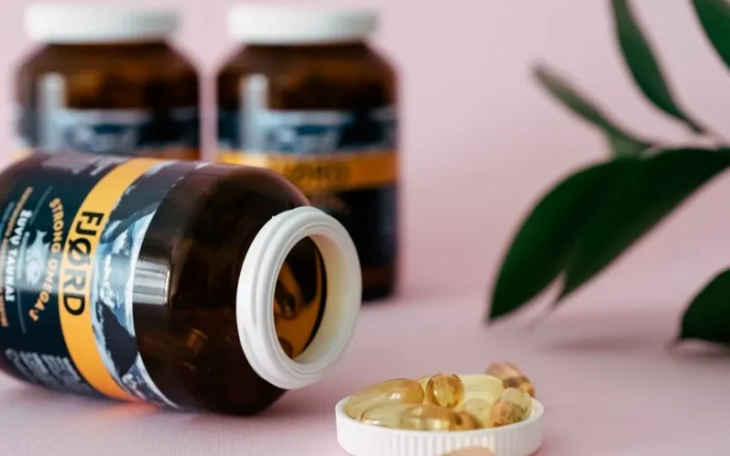 Close-up of omega-3 capsules and bottles on a pink background, ideal for health and wellness themes.
