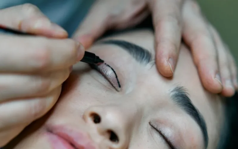 A close-up image of a makeup artist applying eyeliner to a woman's eyelid with precision.
