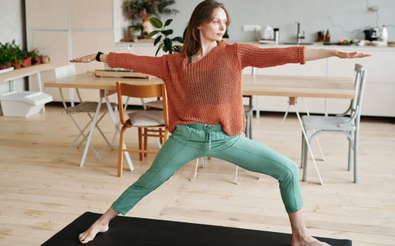 Woman performing a yoga pose in a contemporary home dining area, promoting a healthy lifestyle.