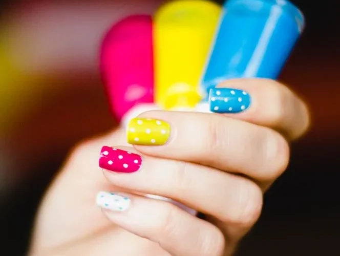 Close-up of colorful polka dot nail art on hand, showcasing pink, yellow, and blue shades.